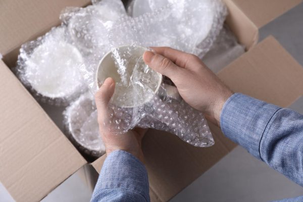 man-covering-ceramic-dishware-with-bubble-wrap-closeup_1339860-791