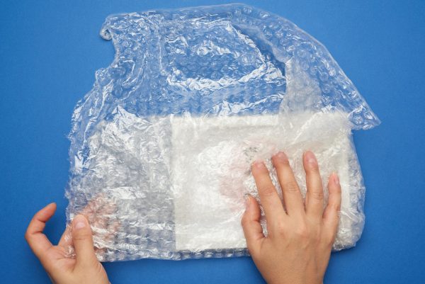 two-female-hands-are-wrapping-item-transparent-plastic-wrap-with-bubbles-blue-background_1048944-12000643